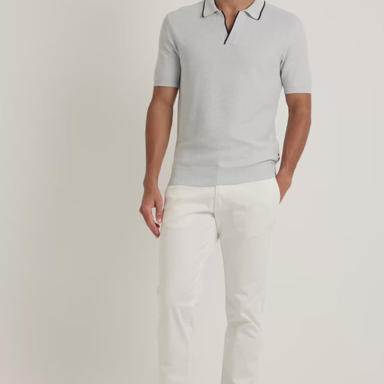 Man wearing light blue polo shirts with black trim with white trousers on a plain background