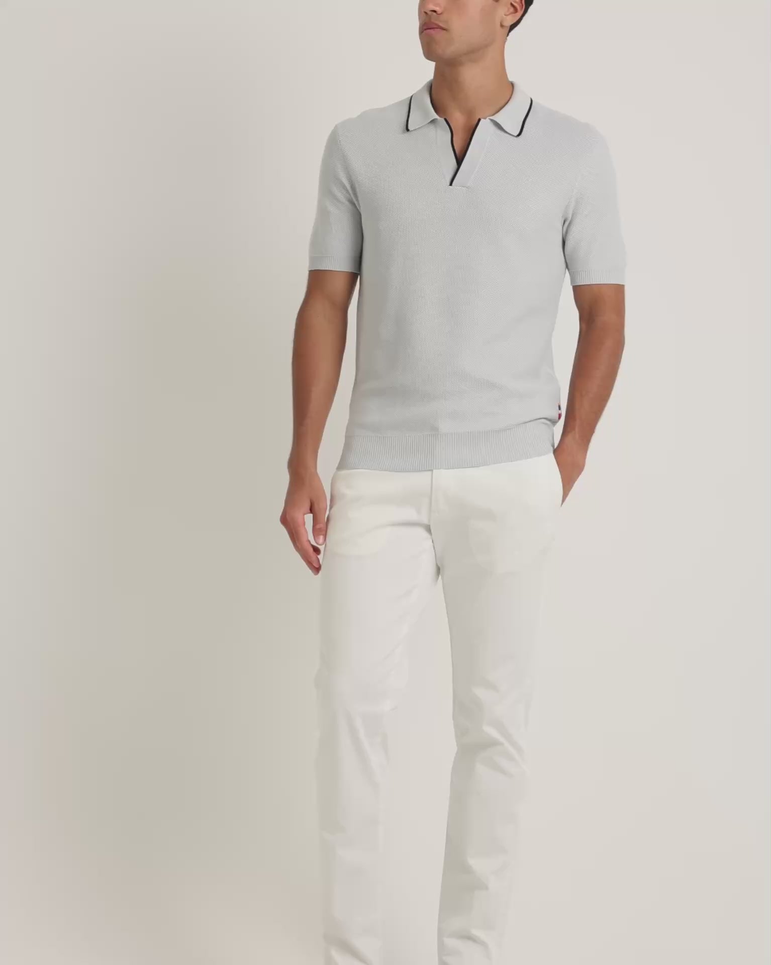 Man wearing light blue polo shirts with black trim with white trousers on a plain background