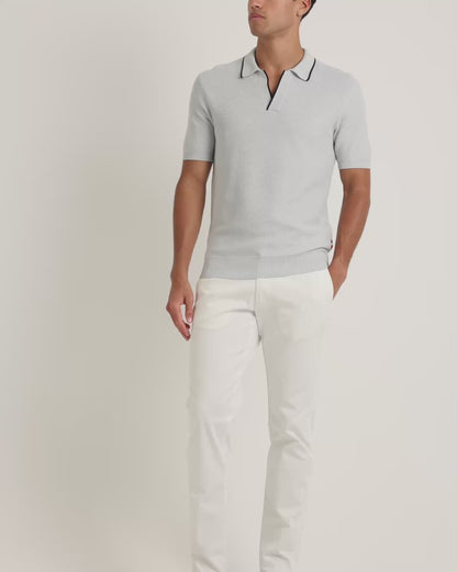 Man wearing light blue polo shirts with black trim with white trousers on a plain background