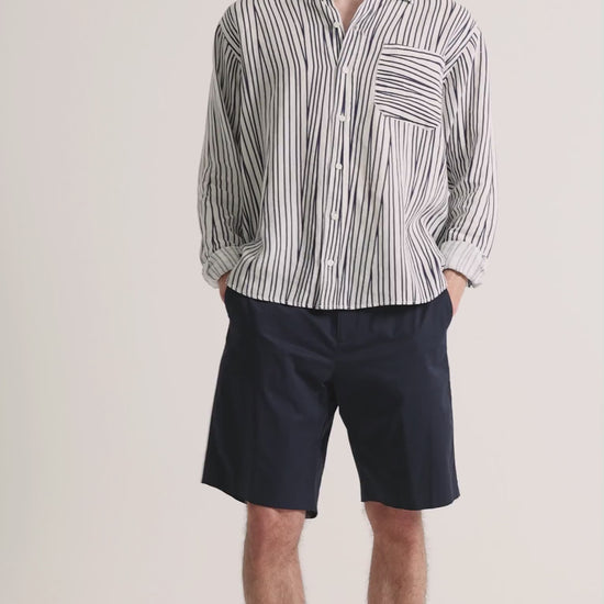 Man wearing printed striped linen shirt with navy shorts on a plain background