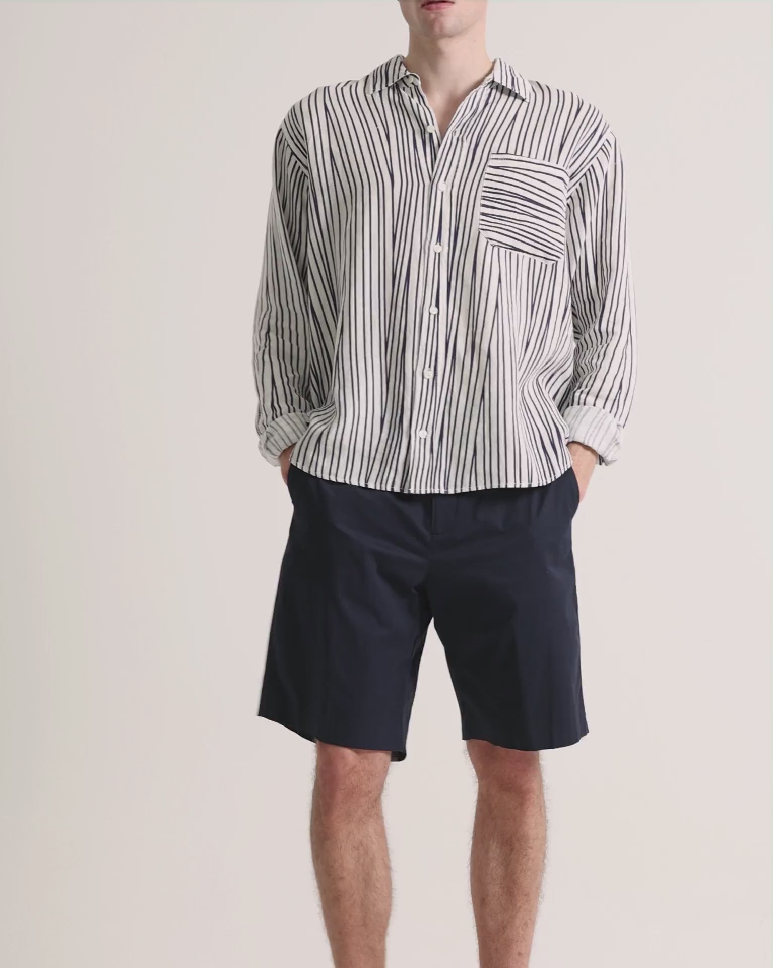 Man wearing printed striped linen shirt with navy shorts on a plain background