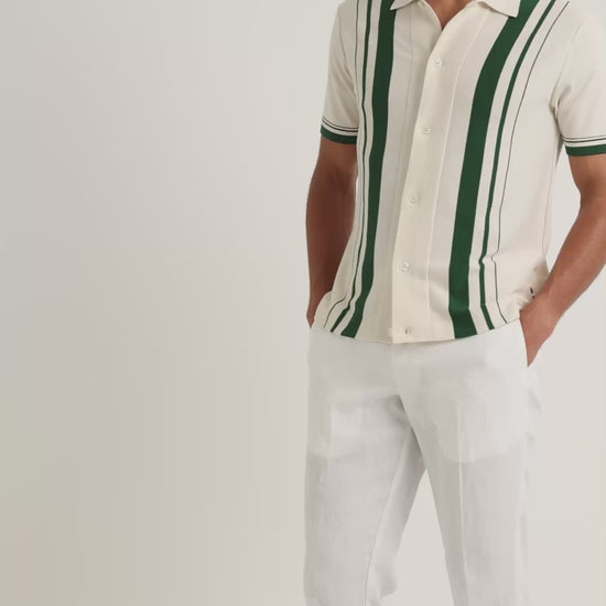 Man wearing light beige shirt with green stripe detail with white trousers on a plain background