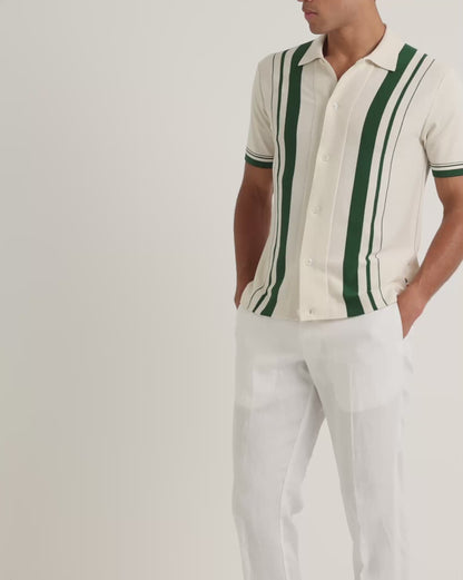 Man wearing light beige shirt with green stripe detail with white trousers on a plain background