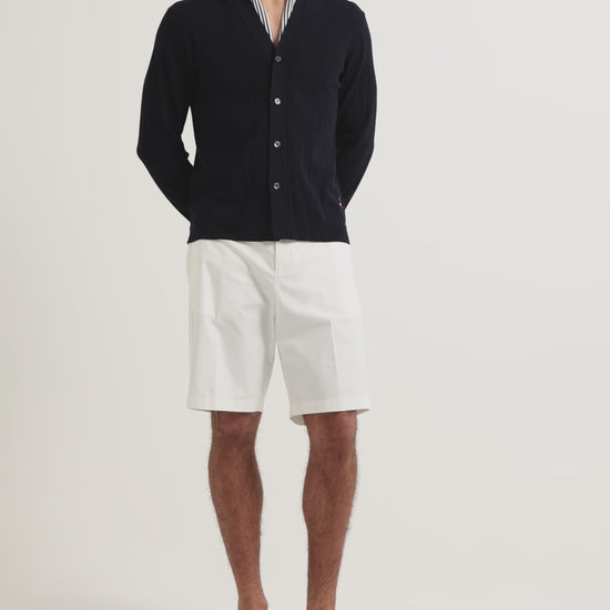 Man wearing knee length white shorts with navy button up cardigan