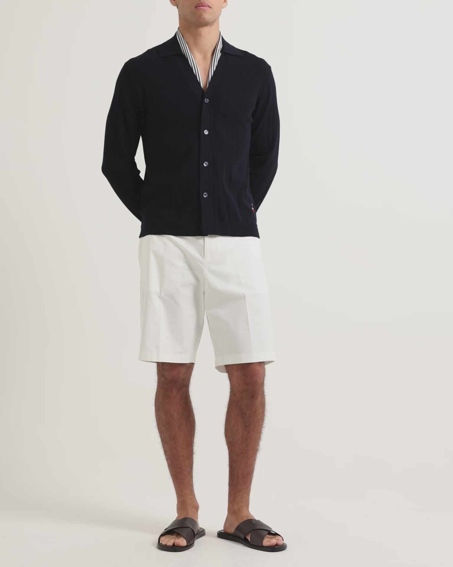 Man wearing knee length white shorts with navy button up cardigan