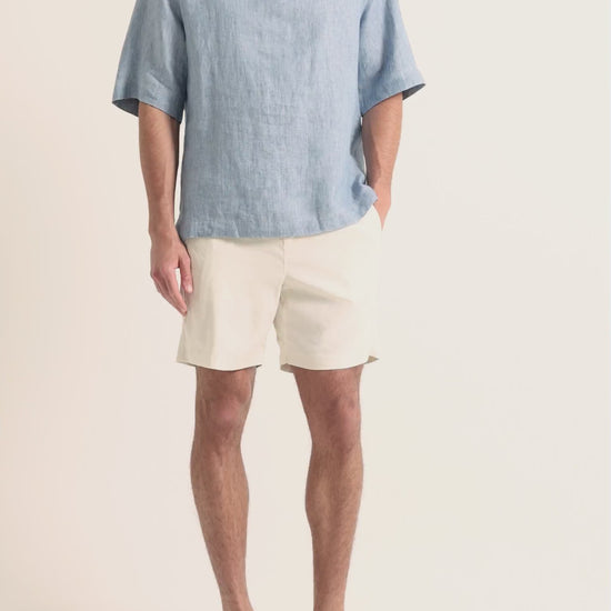 Man wearing blue linen shirt with beige shorts on a plain background