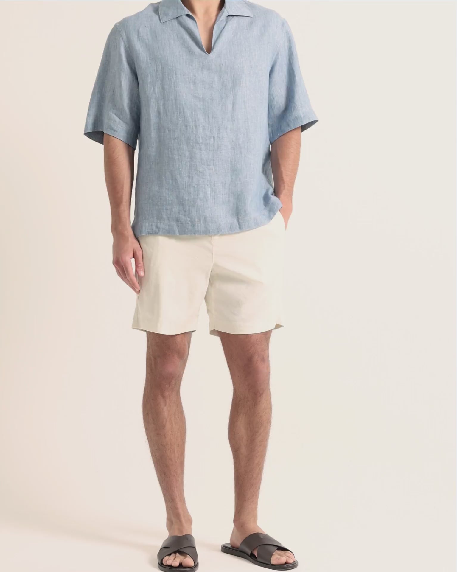 Man wearing blue linen shirt with beige shorts on a plain background