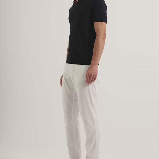 Man wearing navy polo shirt with Ray linen tailored white trousers on a white background