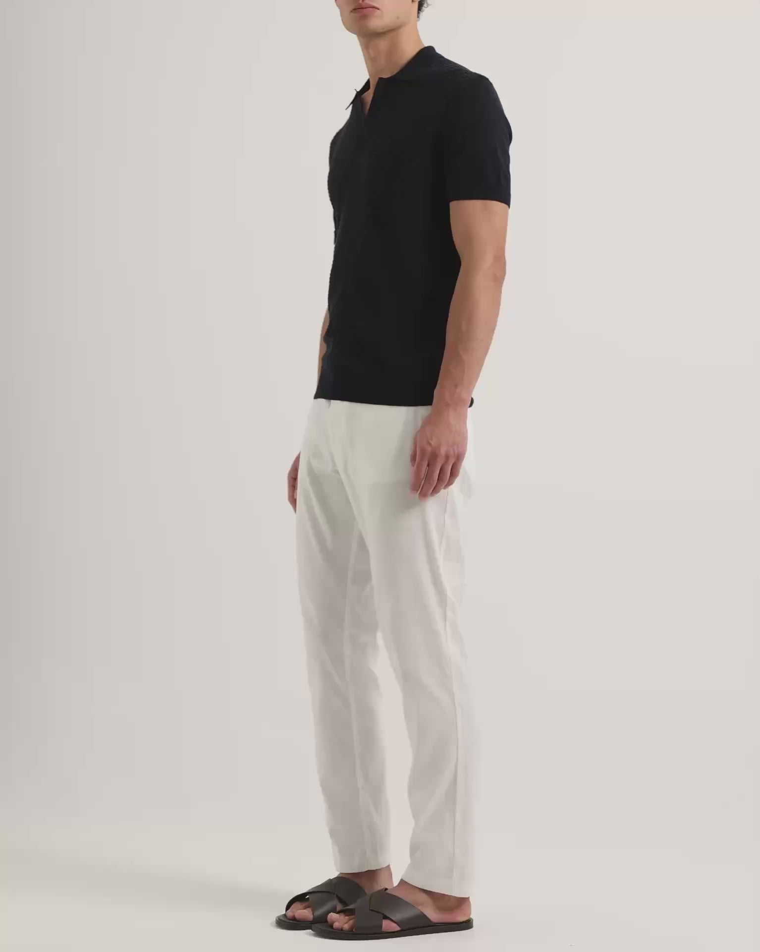 Man wearing navy polo shirt with Ray linen tailored white trousers on a white background