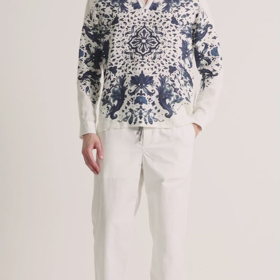 Man wearing printed white linen shirt with white trousers on a plain background