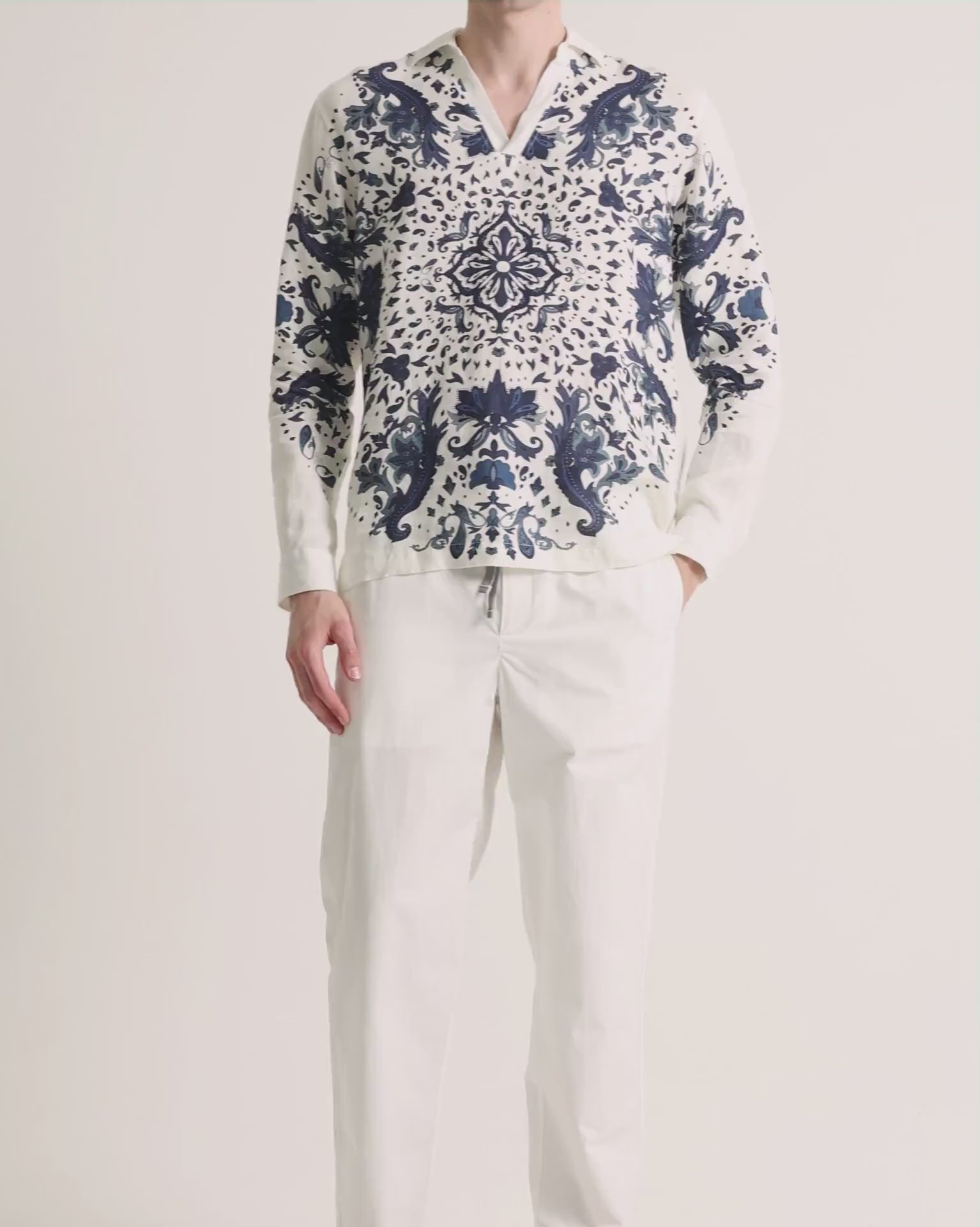 Man wearing printed white linen shirt with white trousers on a plain background