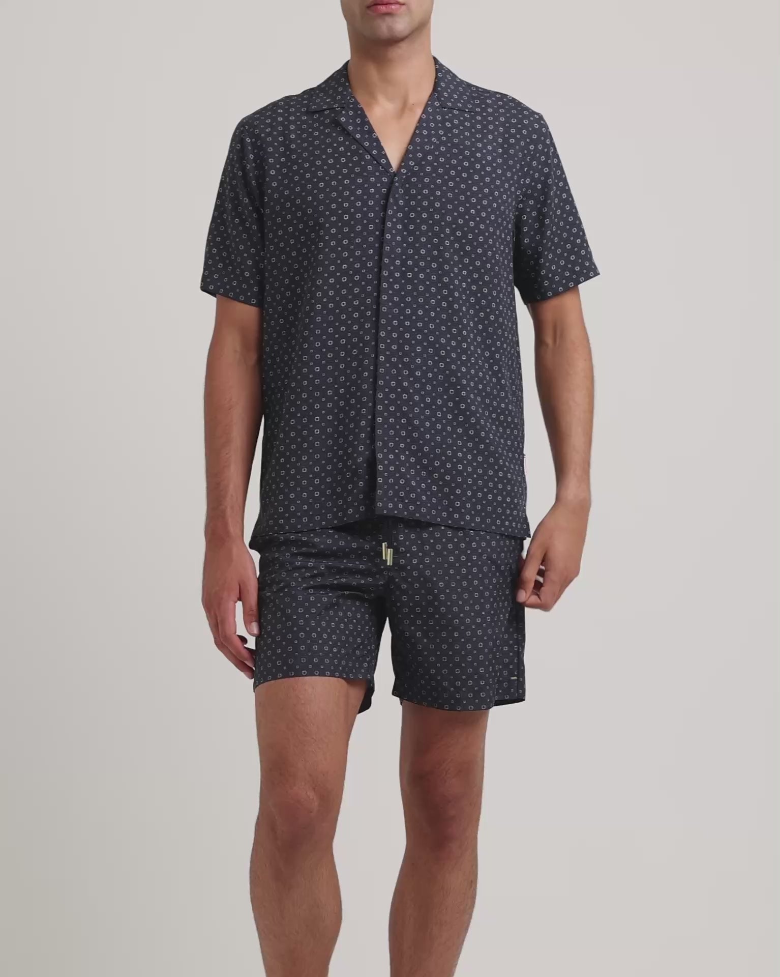 Man wearing navy geometric print shirt with matching swim shorts on a plain background