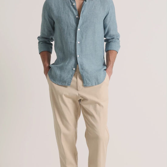 Man wearing blue linen shirt with beige trousers on a plain background