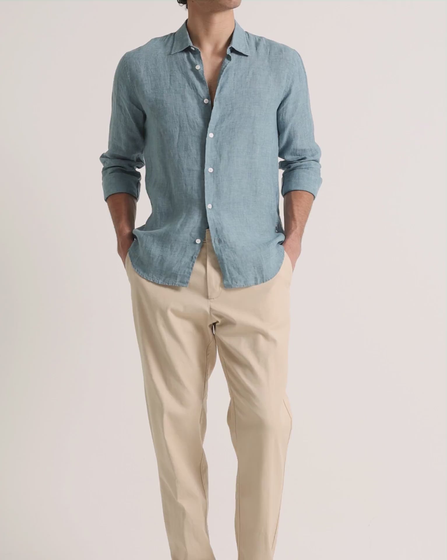 Man wearing blue linen shirt with beige trousers on a plain background