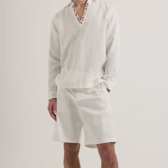Man wearing white long sleeve shirt with embroidery detail on collar with knee length white shorts