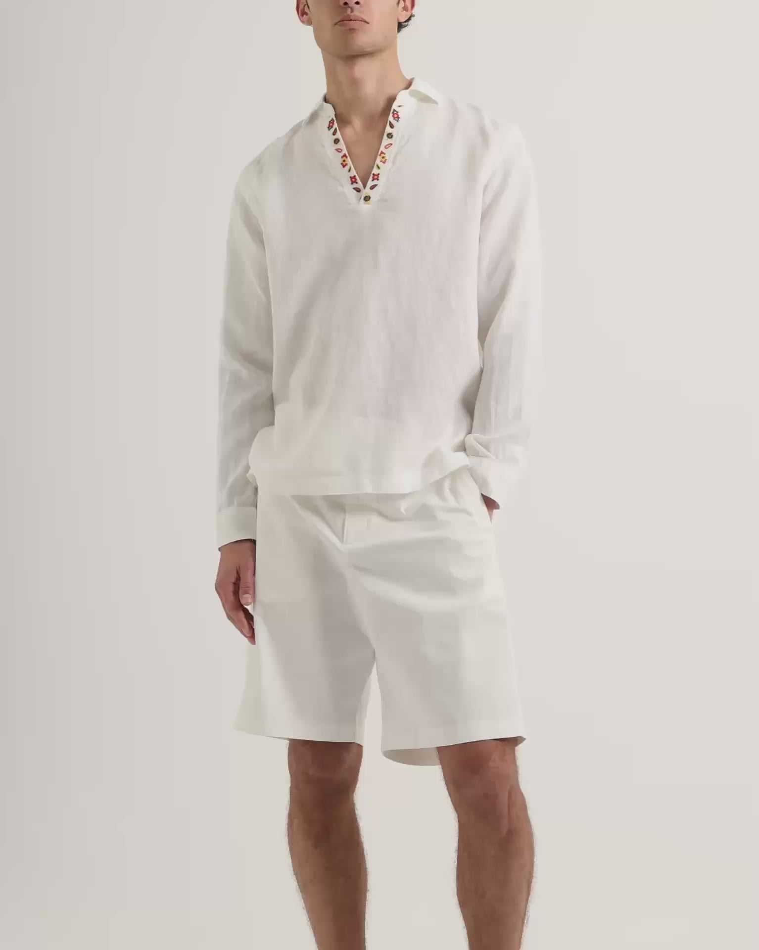 Man wearing white long sleeve shirt with embroidery detail on collar with knee length white shorts