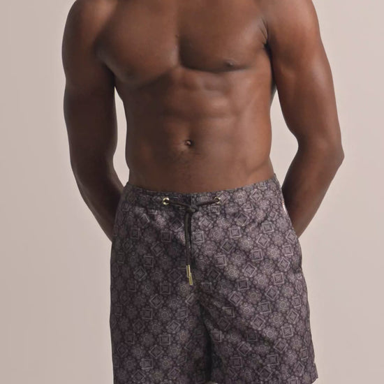 Man wearing dark brown patterned swim shorts with drawstring waist against a plain background
