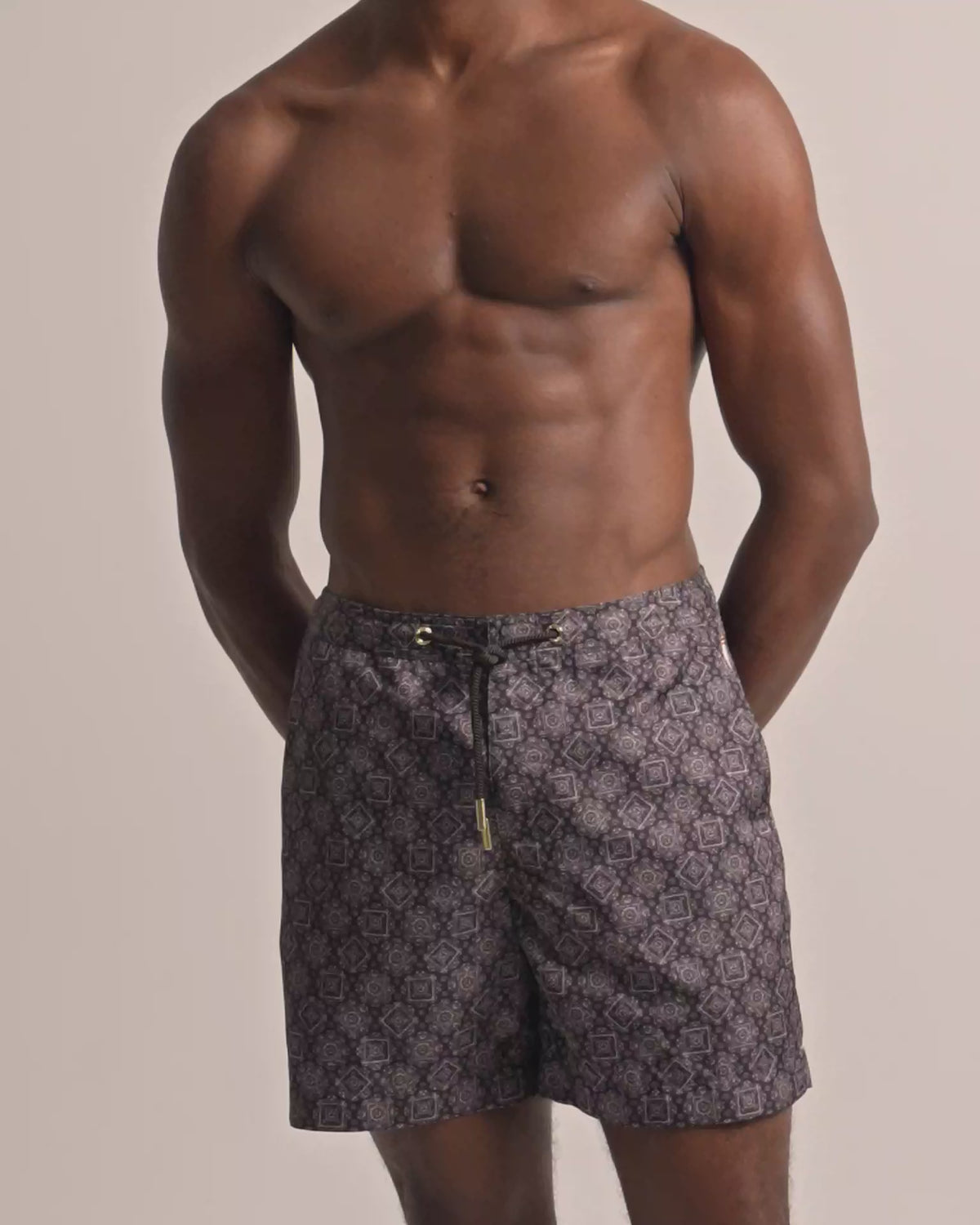 Man wearing dark brown patterned swim shorts with drawstring waist against a plain background
