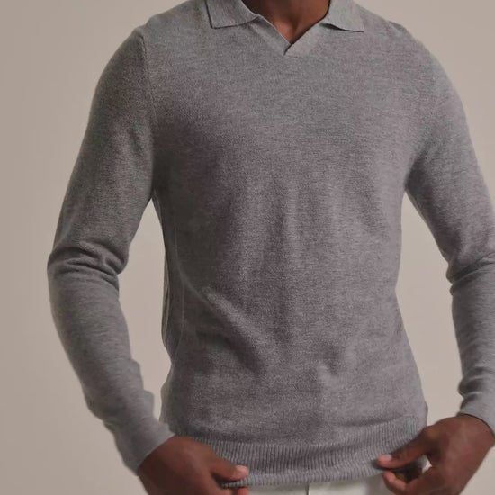Man wearing grey sweater with light trousers against a plain background 