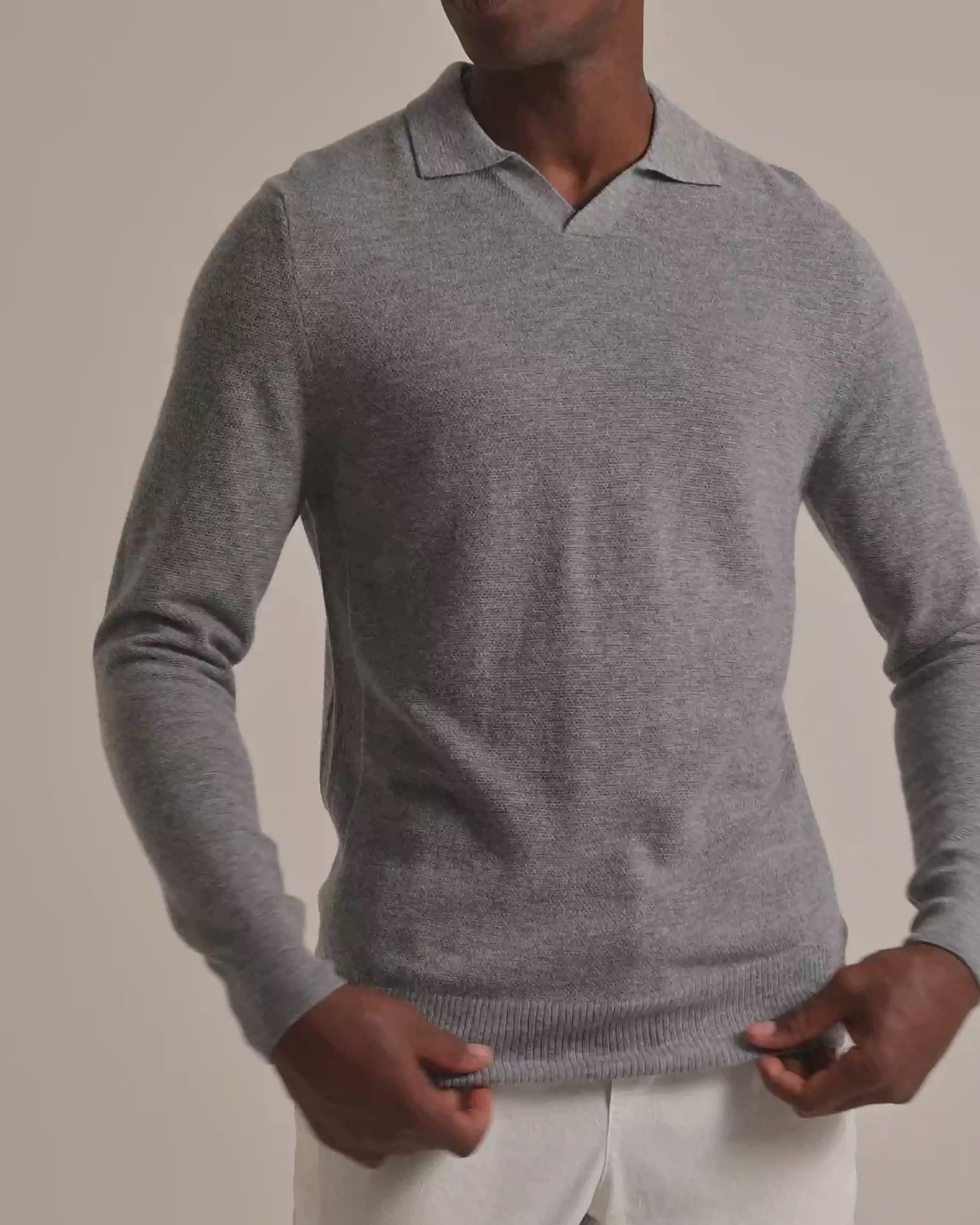 Man wearing grey sweater with light trousers against a plain background 