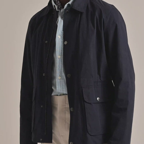 Man wearing a navy field jacket with light blue button up shirt and neckerchief. Modelling against a plain background
