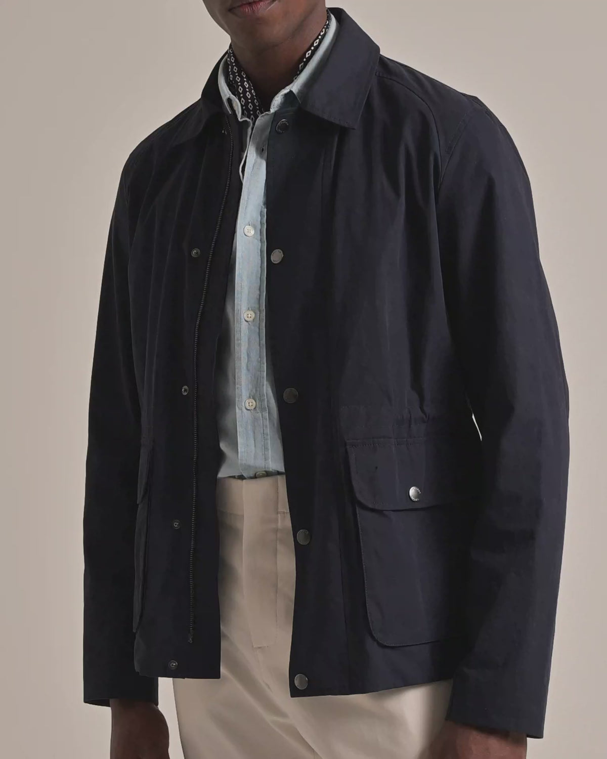 Man wearing a navy field jacket with light blue button up shirt and neckerchief. Modelling against a plain background