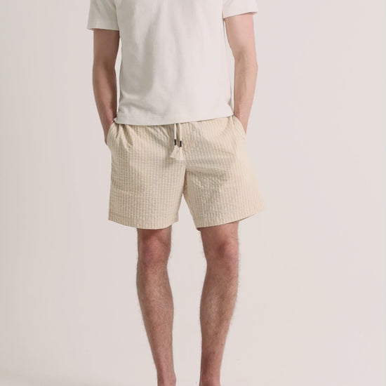 Man wearing light beige polo shirt with striped shorts on a plain background