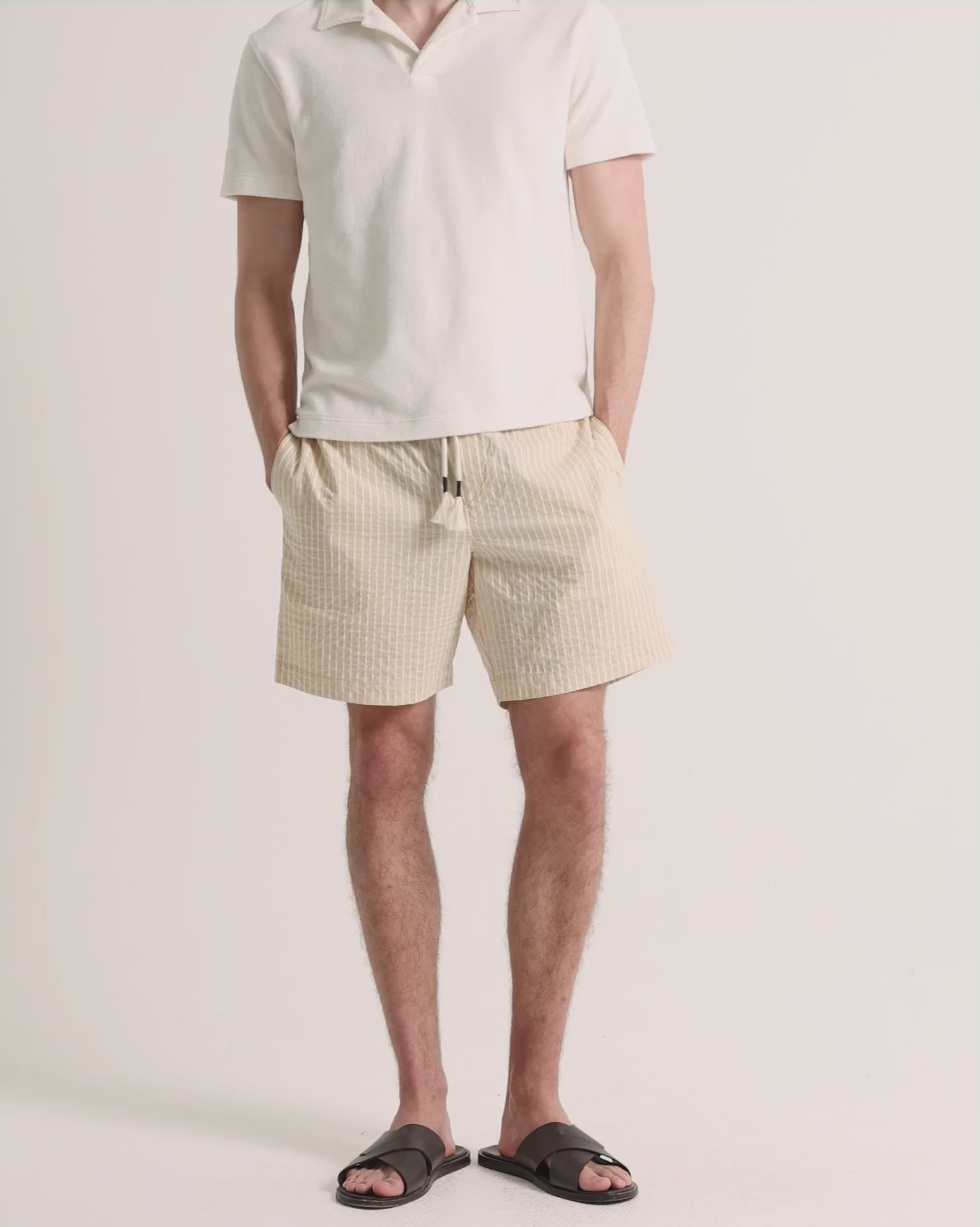 Man wearing light beige polo shirt with striped shorts on a plain background