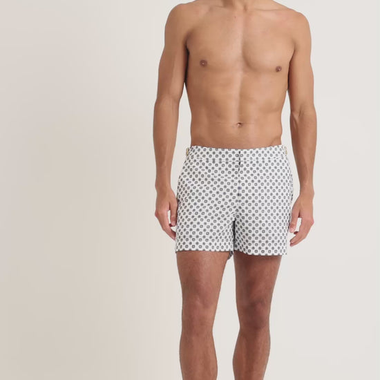 Man wearing white geometric print swim shorts on a plain background