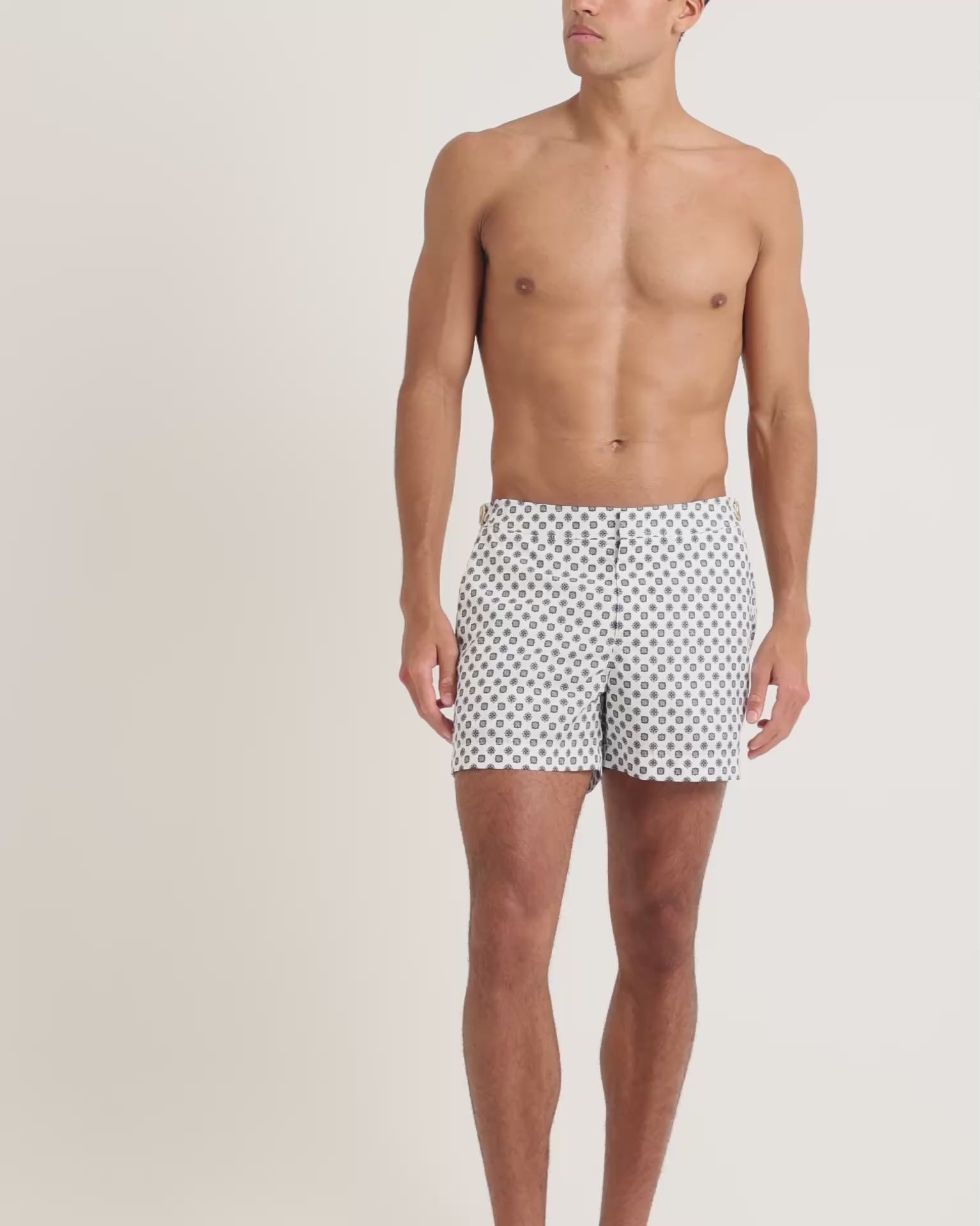 Man wearing white geometric print swim shorts on a plain background