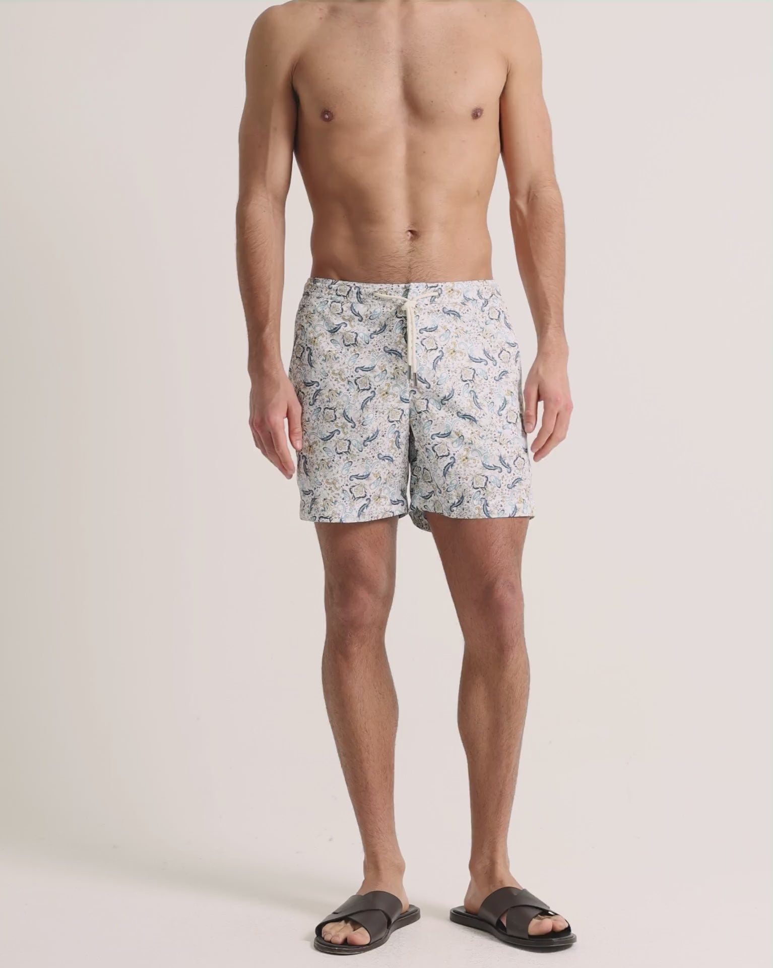 Man wearing blue printed drawcord swim shorts on a plain background