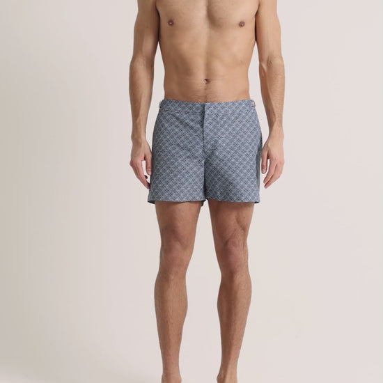 Man wearing navy printed swim shorts on a plain background