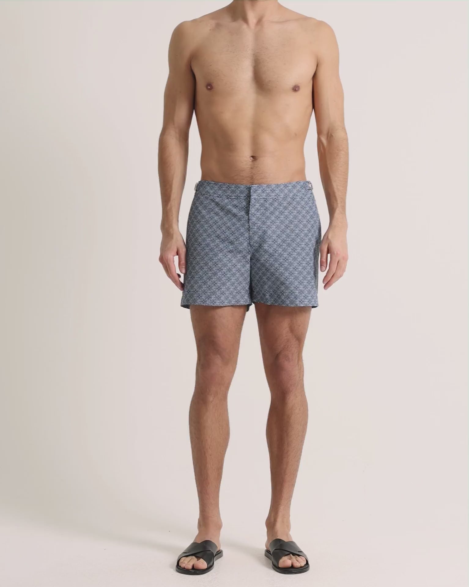 Man wearing navy printed swim shorts on a plain background