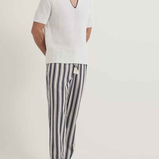 Man wearing white crochet stitch polo shirt with striped linen trousers