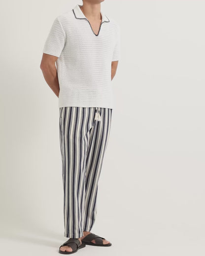 Man wearing white crochet stitch polo shirt with striped linen trousers