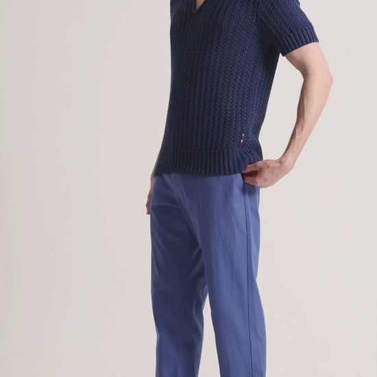 Man wearing navy knitted polo shirt with blue trousers on a plain background