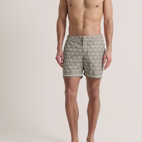 Man wearing beige printed swim shorts on a plain background
