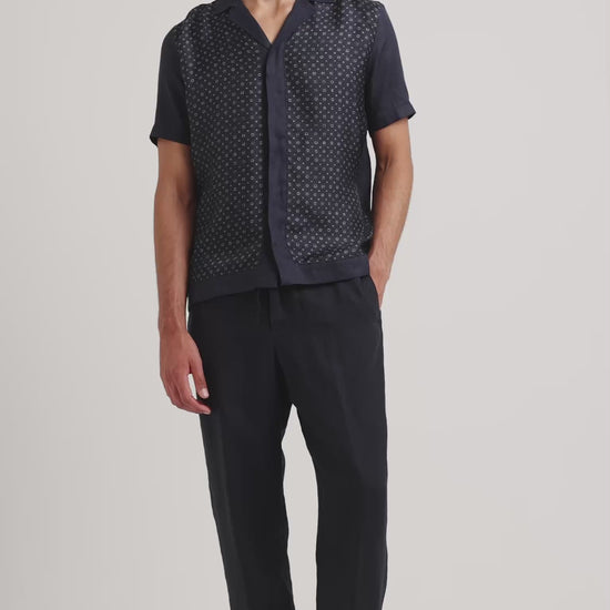 Man wearing navy printed shirt with black trousers on a plain background