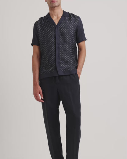 Man wearing navy printed shirt with black trousers on a plain background