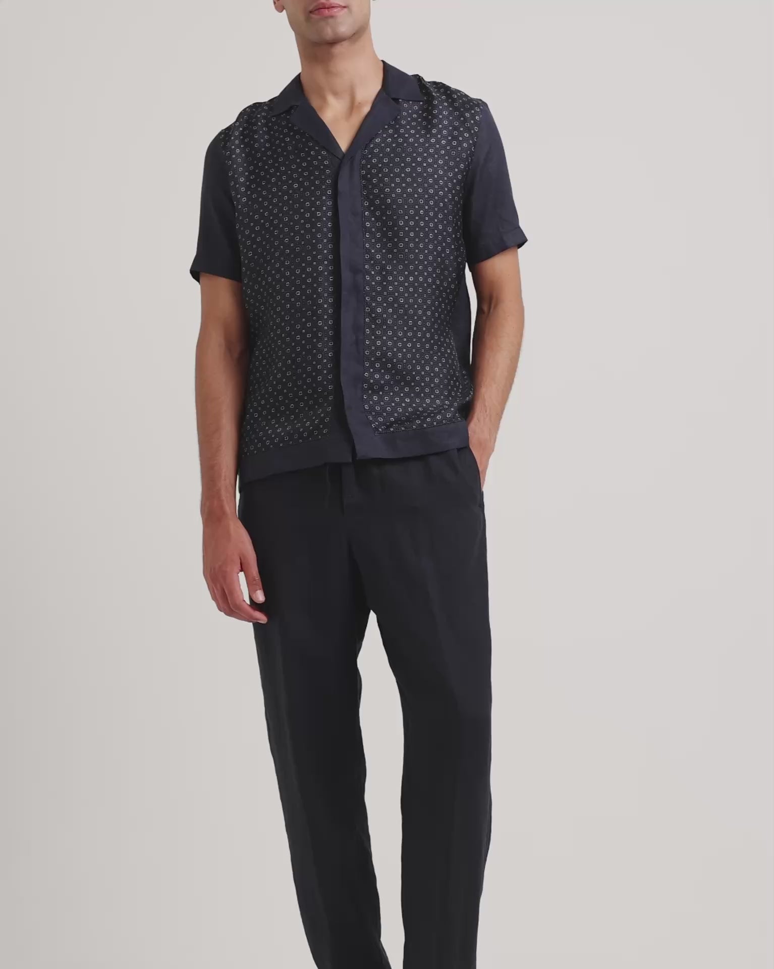 Man wearing navy printed shirt with black trousers on a plain background