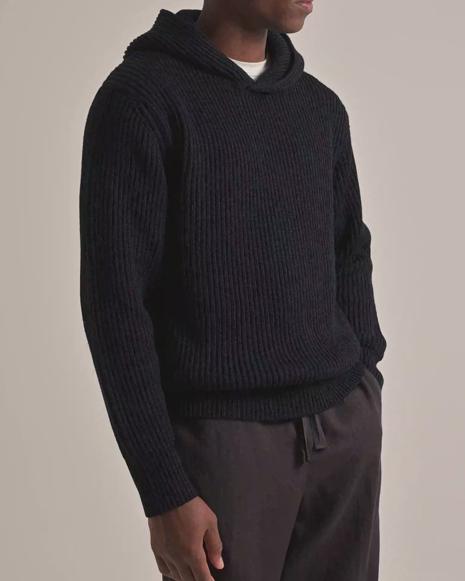 Man wearing navy knitted hoodie with brown trousers on a plain background