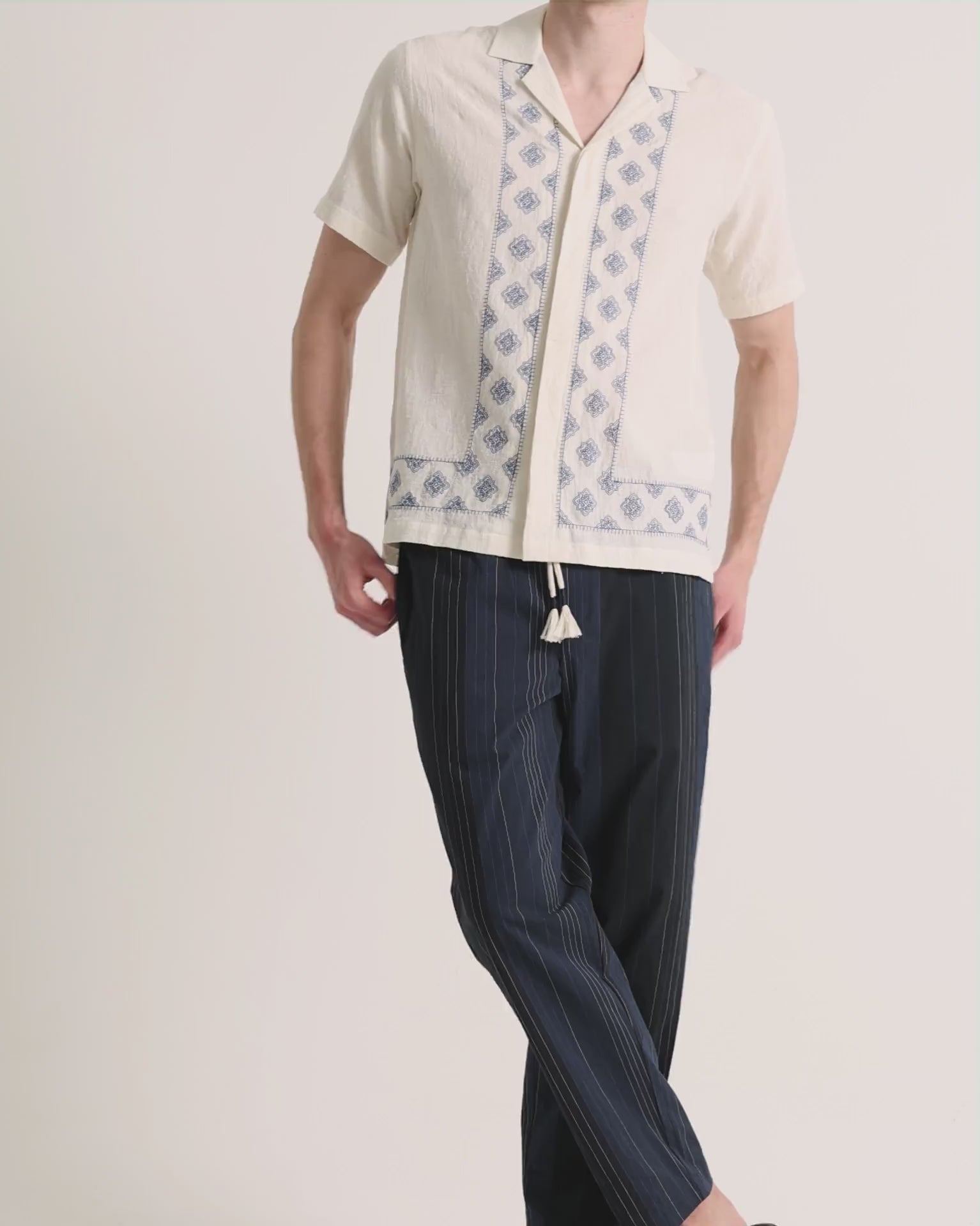 Man wearing printed white linen shirt with navy trousers on a plain background