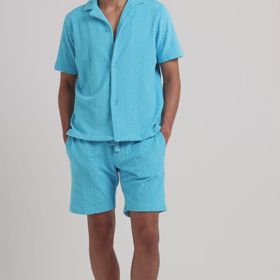 Man wearing blue towelling matching shirt and shorts on a plain background