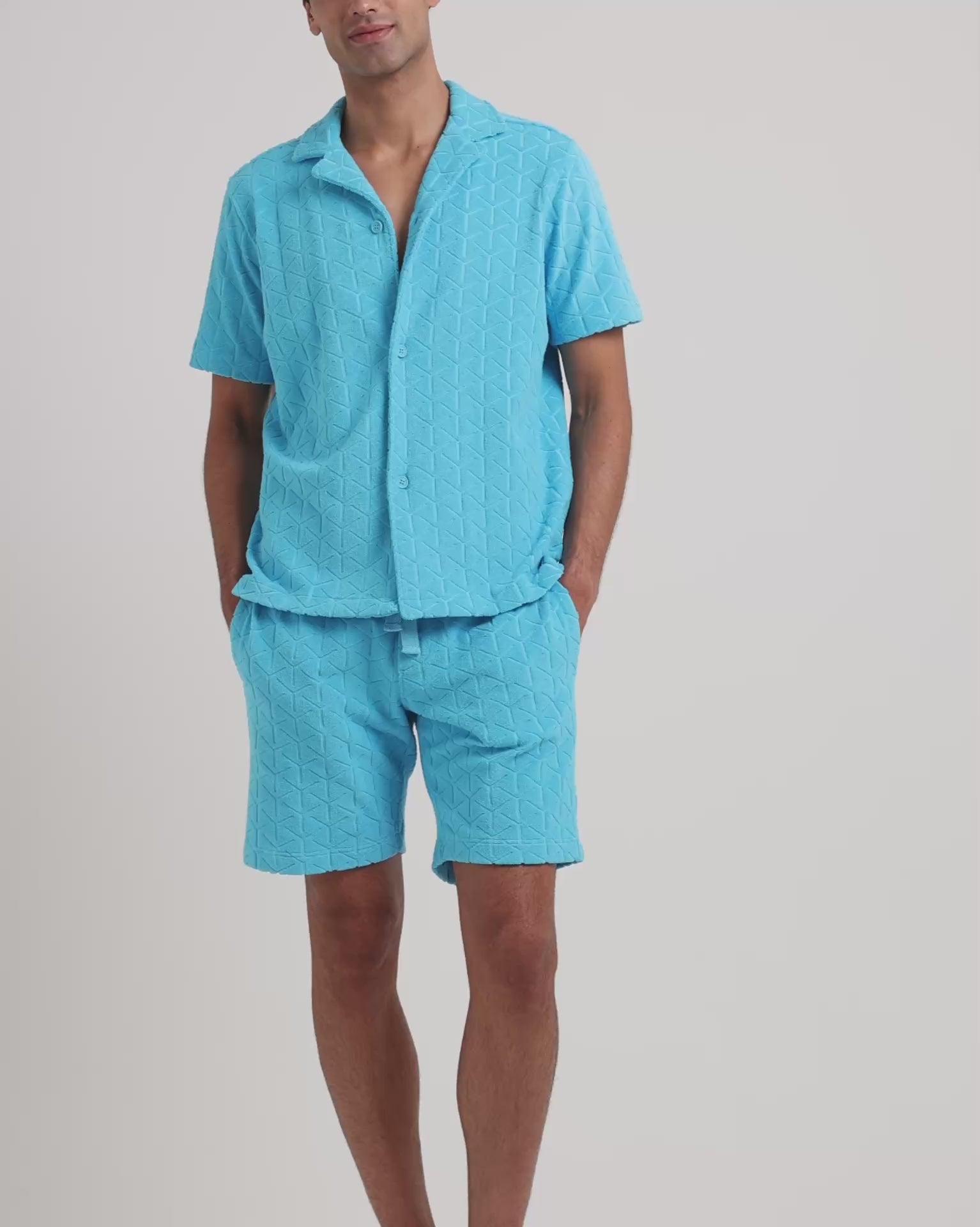 Man wearing blue towelling matching shirt and shorts on a plain background