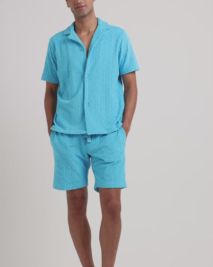 Man wearing blue towelling matching shirt and shorts on a plain background
