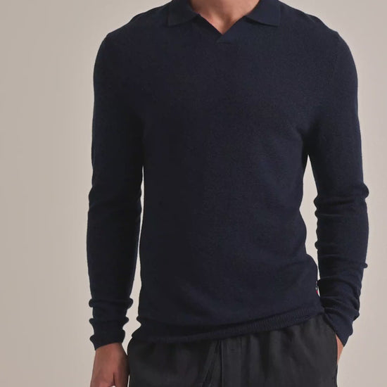 Man wearing navy knitted jumper with dark trousers on a plain background