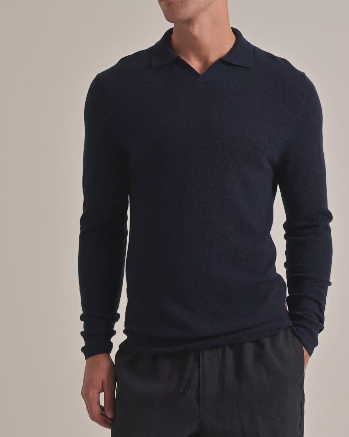 Man wearing navy knitted jumper with dark trousers on a plain background