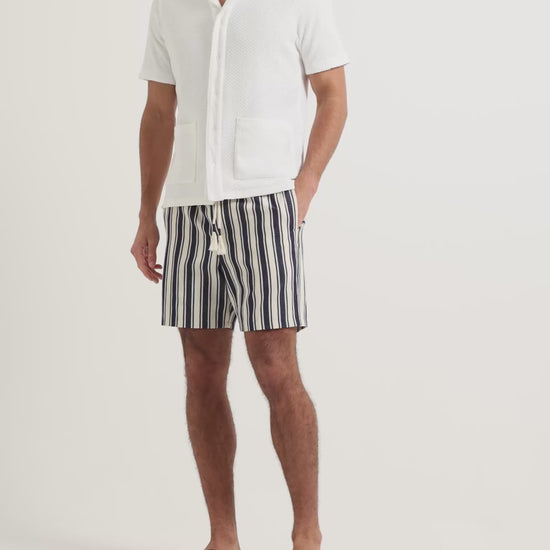 Man wearing white towelling button up shirt and navy and white striped linen shorts