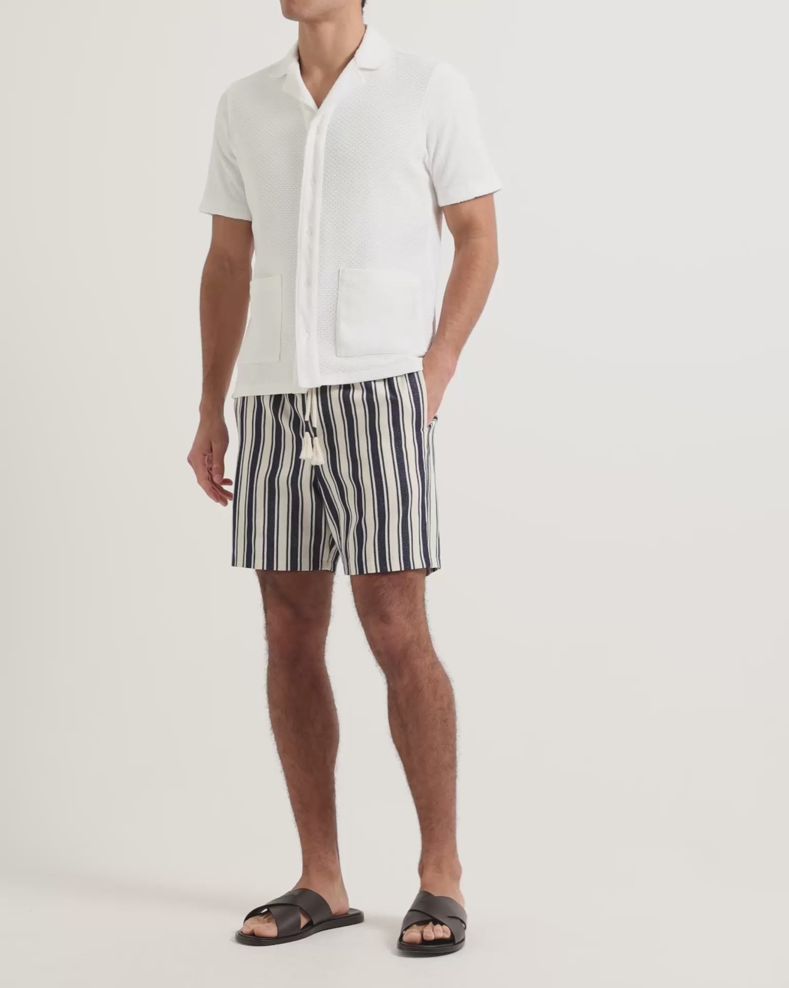 Man wearing white towelling button up shirt and navy and white striped linen shorts