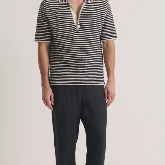 Man wearing navy crochet polo shirt with navy trousers on a plain background